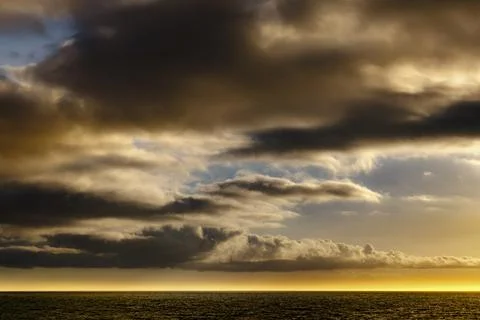Dramatic sunset clouds over a dark ocean horizon with golden light Fotos de archivo