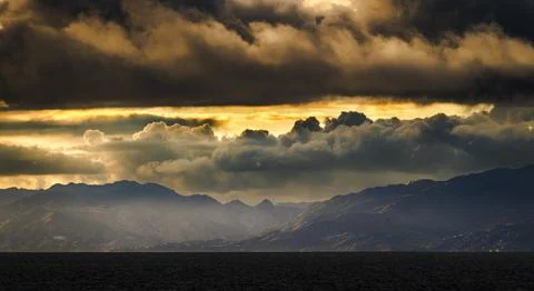 Dramatic sunset clouds over a mountainous coastline with dark ocean waves Fotos de archivo