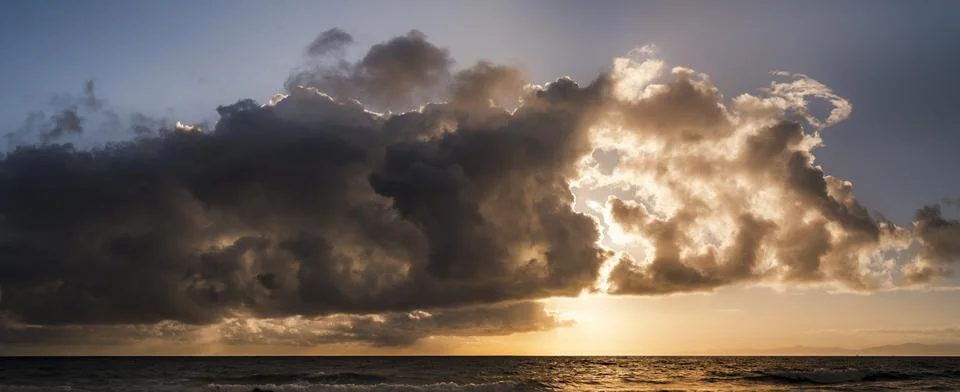 Dramatic sunset clouds over the ocean with golden light breaking through Foto stock