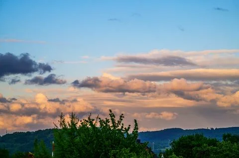 Dramatic sunset clouds paint the sky with warm hues over rolling green hills Stock Photos