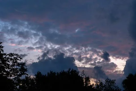 Dramatic sunset clouds with pink glow in evening sky above forest silhouette Stock Photos