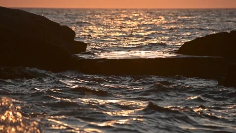Dramatic sunset colors at sea. Waves hit the rocky shore in the foreground Stock Footage 139223388