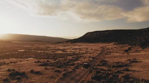 Dramatic sunset footage following a car on a western dirt road with mountains Stock Footage 128660656