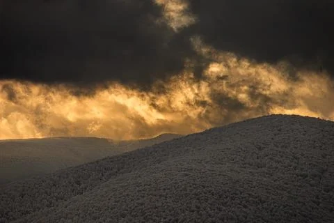 Dramatic sunset light breaking through dark storm clouds over snow-covered .. Stock Photos