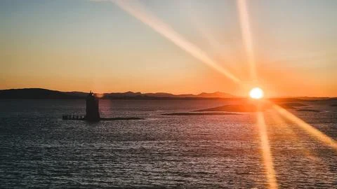 Dramatic sunset with lighthouse silhouette and sunbeams Stock Photos