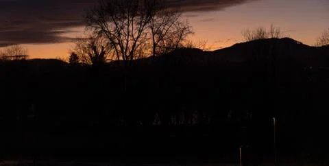 Dramatic sunset with lilac orange clouds over bar trees and hills in winterti Stock Photos