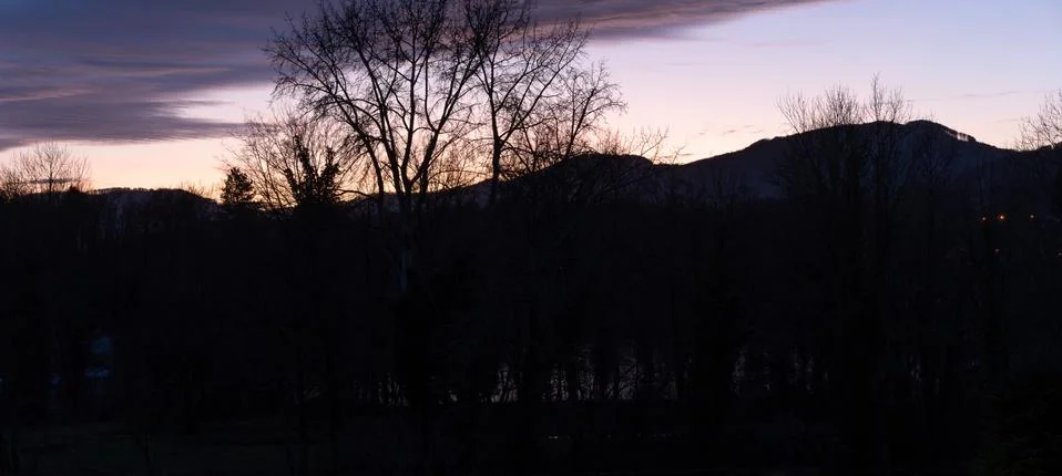 Dramatic sunset with lilac orange clouds over bar trees and hills in winterti Stock Photos