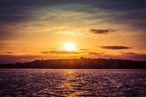 Dramatic sunset over calm bay waters with hilly coast at the distance. Stock Photos
