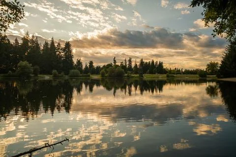 A dramatic sunset over a calm lake with clouds reflecting in the water and si Foto stock