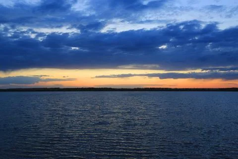 Dramatic sunset over calm water with deep blue clouds and orange horizon Stock-Fotos