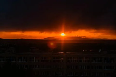 A dramatic sunset over a city skyline. The sun sets behind dark clouds, casti Stock Photos