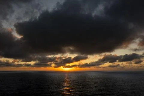 Dramatic sunset over the dark ocean with heavy clouds and golden light refl.. Fotos de archivo