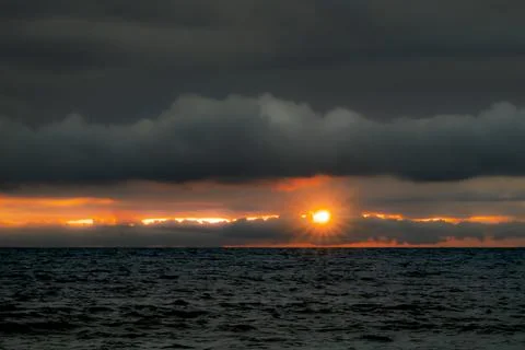 Dramatic sunset over dark ocean waves with sunburst through clouds Photos