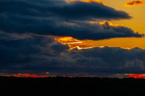 Dramatic sunset over a dark silhouette of trees with vibrant orange and yel.. Stock Photos
