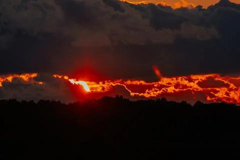 Dramatic sunset over a dark silhouette of trees with vibrant orange and red.. Fotos de archivo