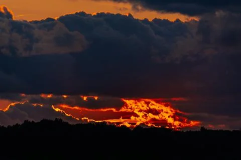Dramatic sunset over a dark silhouette of trees with vibrant orange and red.. Stock-Fotos