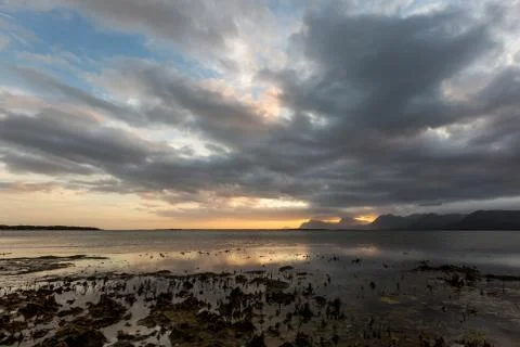 Dramatic sunset over lake and mountain range under dramatic clouds Stock Photos