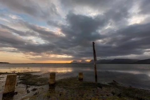 Dramatic sunset over lake and mountain range under dramatic clouds Stock Photos