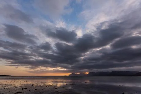 Dramatic sunset over lake and mountain range under dramatic clouds Stock Photos