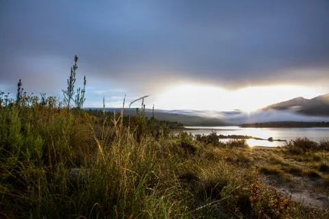 Dramatic sunset over lake and mountain range under dramatic clouds Stock Photos