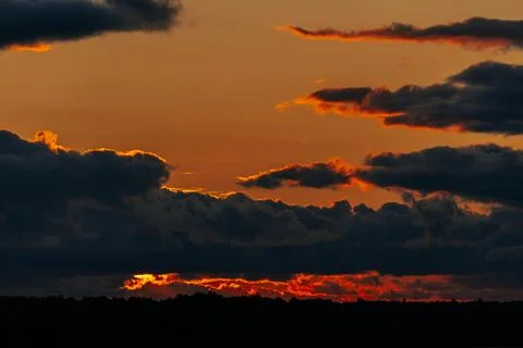 Dramatic sunset over a landscape with dark clouds and vibrant orange and re.. Stock Photos