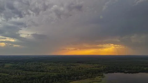 Dramatic sunset over a lush forest landscape with a serene lake. Dark clouds Stock Photos