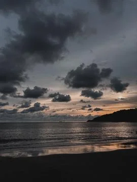 Dramatic sunset over Malaysian beach with dark clouds and calm sea Stock Photos