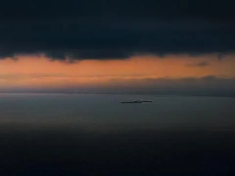 Dramatic sunset over the ocean with cargo ships and a distant airplane 库存照片