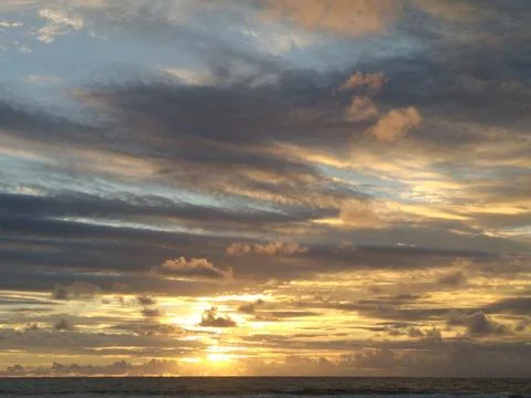 A dramatic sunset over the ocean with clouds reflecting golden light creates  Stock Photos