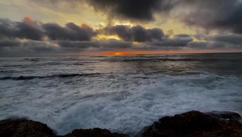 Dramatic sunset over the ocean with crashing waves against rocky shore Vidéo 334084414