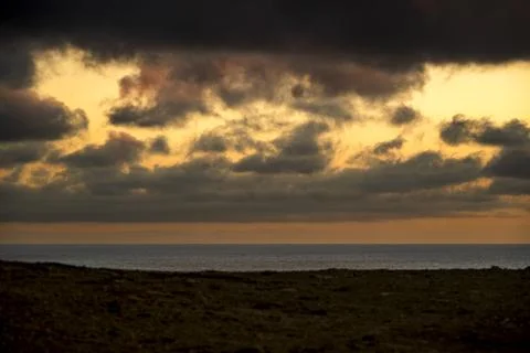 Dramatic sunset over the ocean with dark clouds and golden light breaking t.. Photos