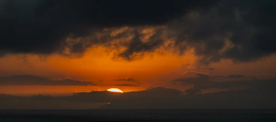 Dramatic sunset over the ocean with dark clouds and vibrant orange sky 库存照片