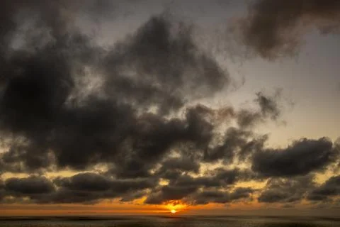 Dramatic sunset over the ocean with dark, moody clouds and vibrant orange hue Fotos de archivo