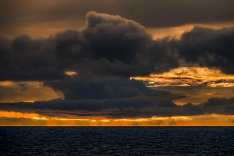 Dramatic sunset over the ocean with dark, moody clouds and vibrant orange sky Fotos de archivo