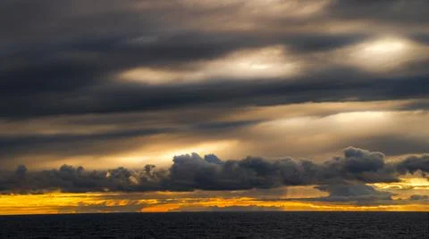 Dramatic sunset over the ocean with dark, textured clouds and golden light .. Fotos de archivo