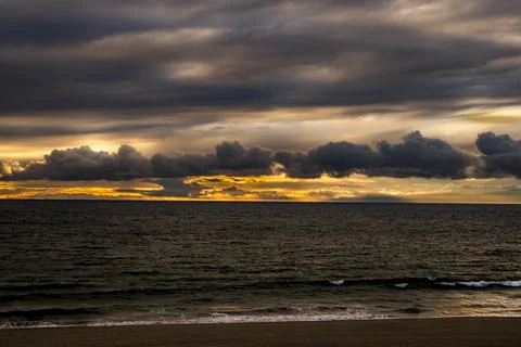 Dramatic sunset over the ocean with dark clouds and golden light breaking t.. Fotos de archivo