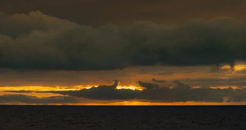 Dramatic sunset over the ocean with dark, moody clouds and vibrant orange sky Fotos de archivo
