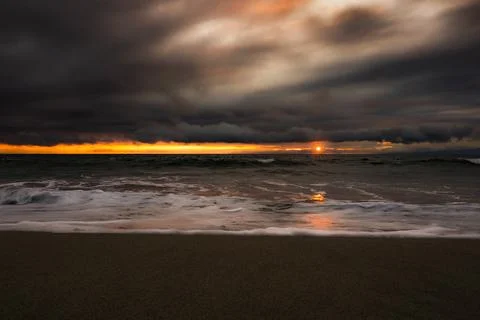 Dramatic sunset over the ocean with dark clouds and glowing horizon line Fotos de archivo