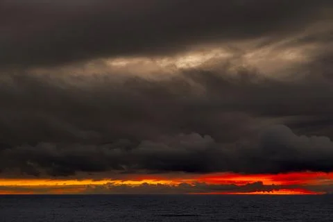 Dramatic sunset over the ocean with dark storm clouds and vibrant orange glow Fotos de archivo