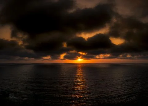 Dramatic sunset over the ocean with dark, moody clouds and golden light ref.. Fotos de archivo