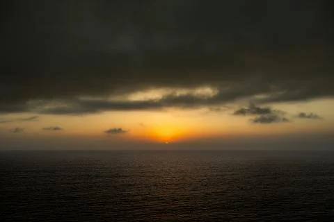 Dramatic sunset over the ocean with dark clouds and golden light reflecting.. Fotos de archivo