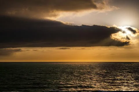 Dramatic sunset over the ocean with dark clouds and golden light rays Fotos de archivo