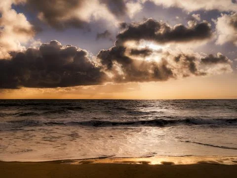 Dramatic sunset over the ocean with dark clouds and golden light breaking t.. Photos