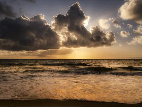 Dramatic sunset over the ocean with dark clouds and golden light breaking t.. Photos