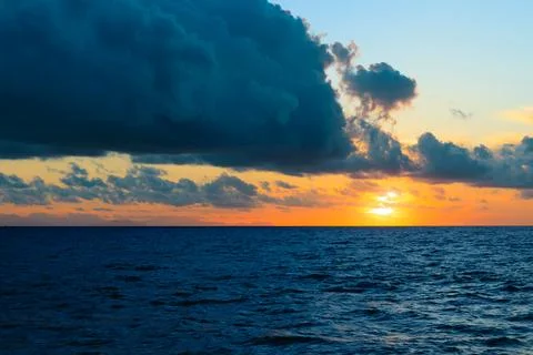Dramatic sunset over the ocean with dark clouds and vibrant sky Stock Photos