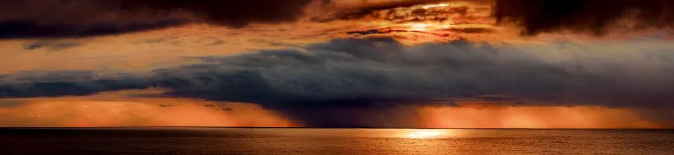 Dramatic sunset over the ocean with dark storm clouds and golden light 스톡 사진