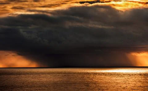 Dramatic sunset over the ocean with dark storm clouds and rain shafts Stock Photos