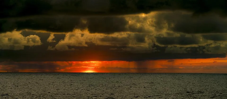 Dramatic sunset over the ocean with dark storm clouds and rain shafts 스톡 사진