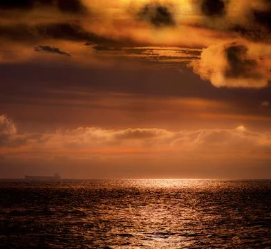 Dramatic sunset over the ocean with a distant cargo ship silhouette Foto stock