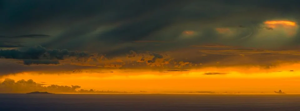 Dramatic sunset over the ocean with distant island and stormy clouds 写真素材